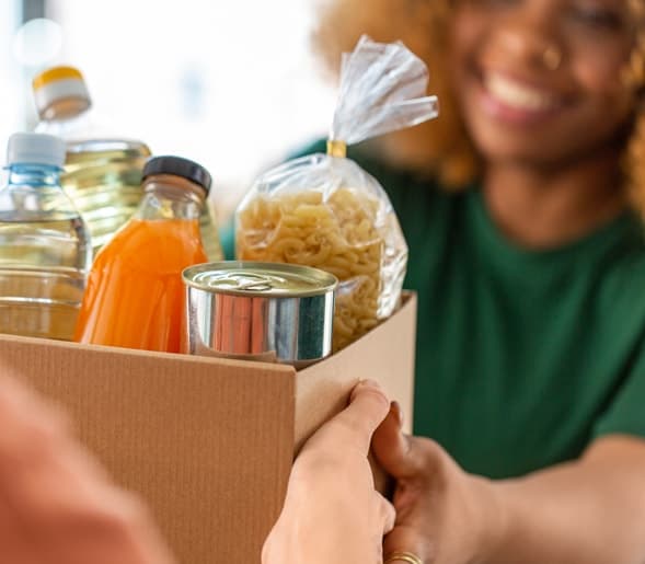 A volunteer handing over a box of pantry food and groceries