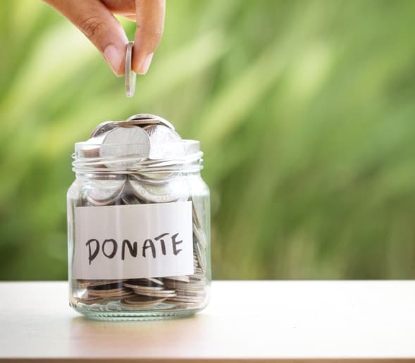A hand placing a coin into a glass jar labeled Donate