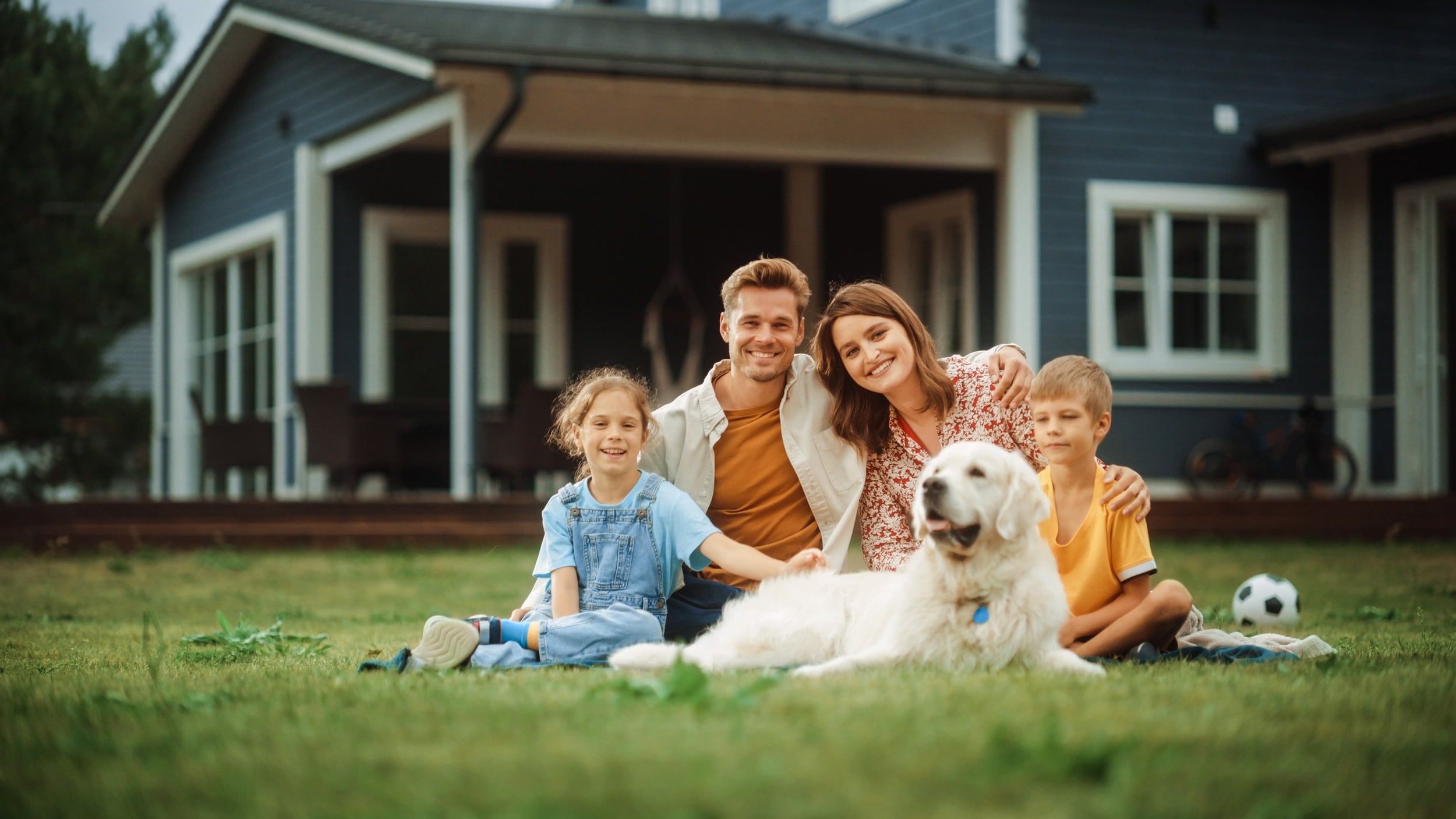A family relaxing with their dog on the front lawn of a renovated home