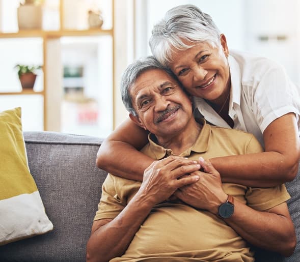 A smiling senior couple embracing on a sofa at home