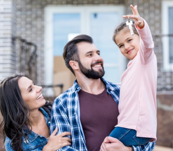 A smiling family in front of a house, the daughter holding up a set of keys