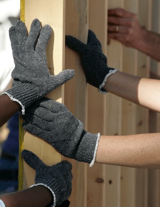 Volunteers in work gloves holding up a wooden wall frame during a home build