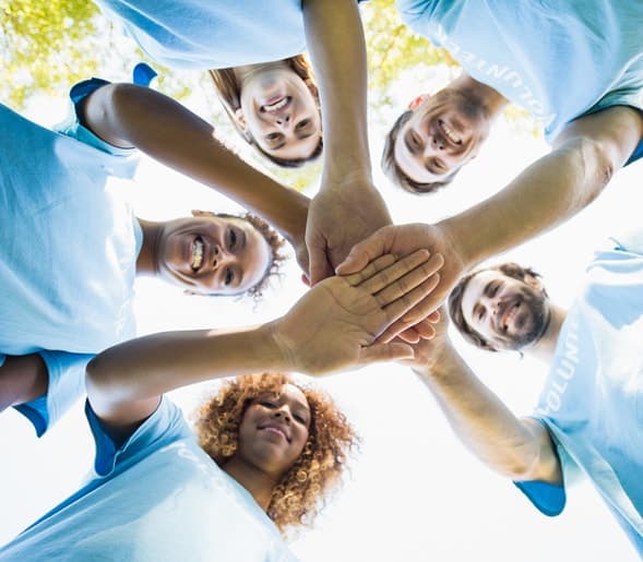Smiling volunteers in matching shirts joining hands in a circle